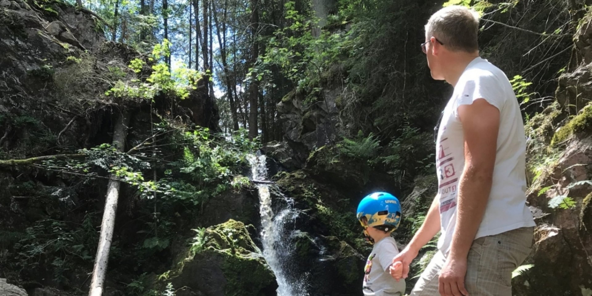 Ein Wanderer betrachtet einen kleinen Wasserfall, der über Felsstufen in ein Becken fließt.