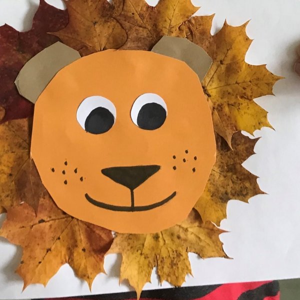 Ein Kind hält ein selbstgebasteltes Bild aus bunten Herbstblättern, das ein Löwengesicht zeigt.