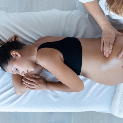 Eine schwangere Frau entspannt bei einer sanften Massage in Seitenlage auf einer Therapieliege.