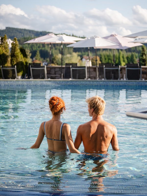 Ein Paar blickt vom Beckenrand des Außenpools auf die malerische Landschaft rund um den Schluchsee.