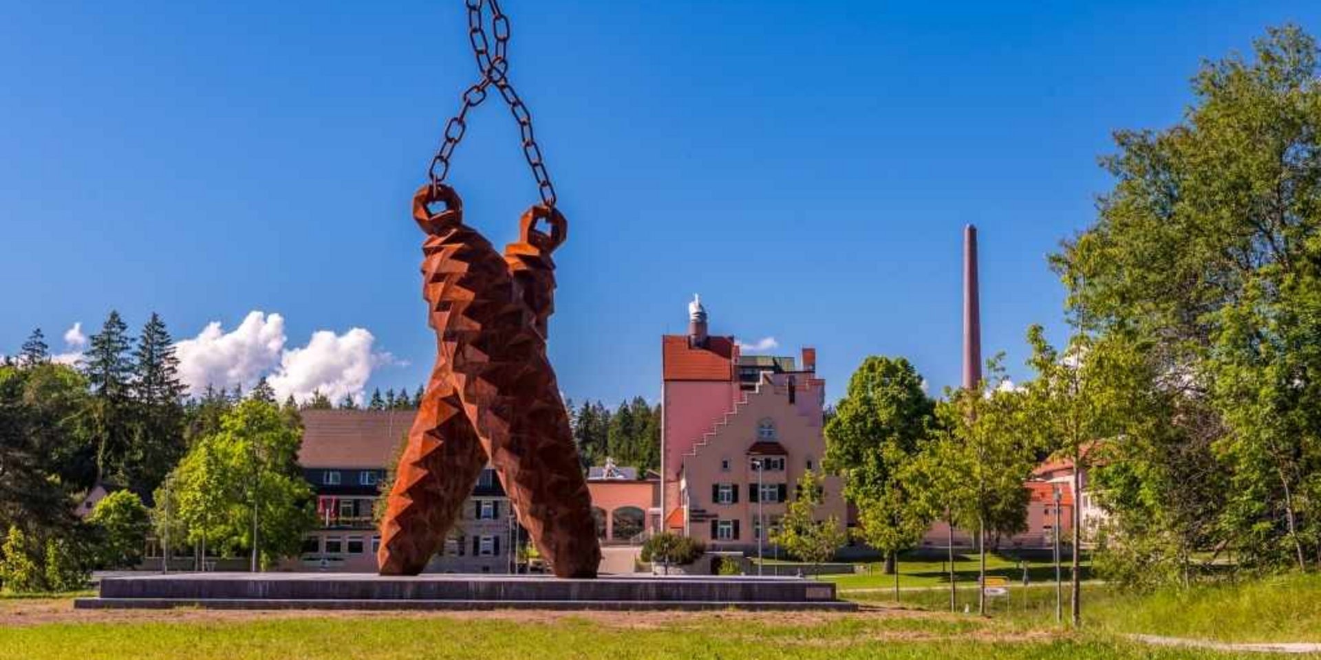 Moderne Skulptur auf einer Wiese vor einem historischen Gebäude im Schwarzwald.