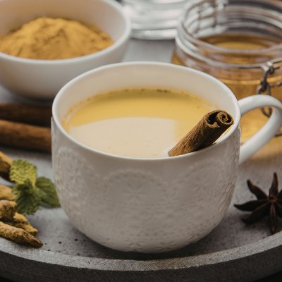 Tee mit einer Zimtstange umgeben von verschiedenen Gewürzen