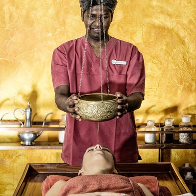 Ein Therapeut hält die Ölschale für einen Stirnguss über einen liegenden Gast im Hotel Vier Jahreszeiten im Schwarzwald.