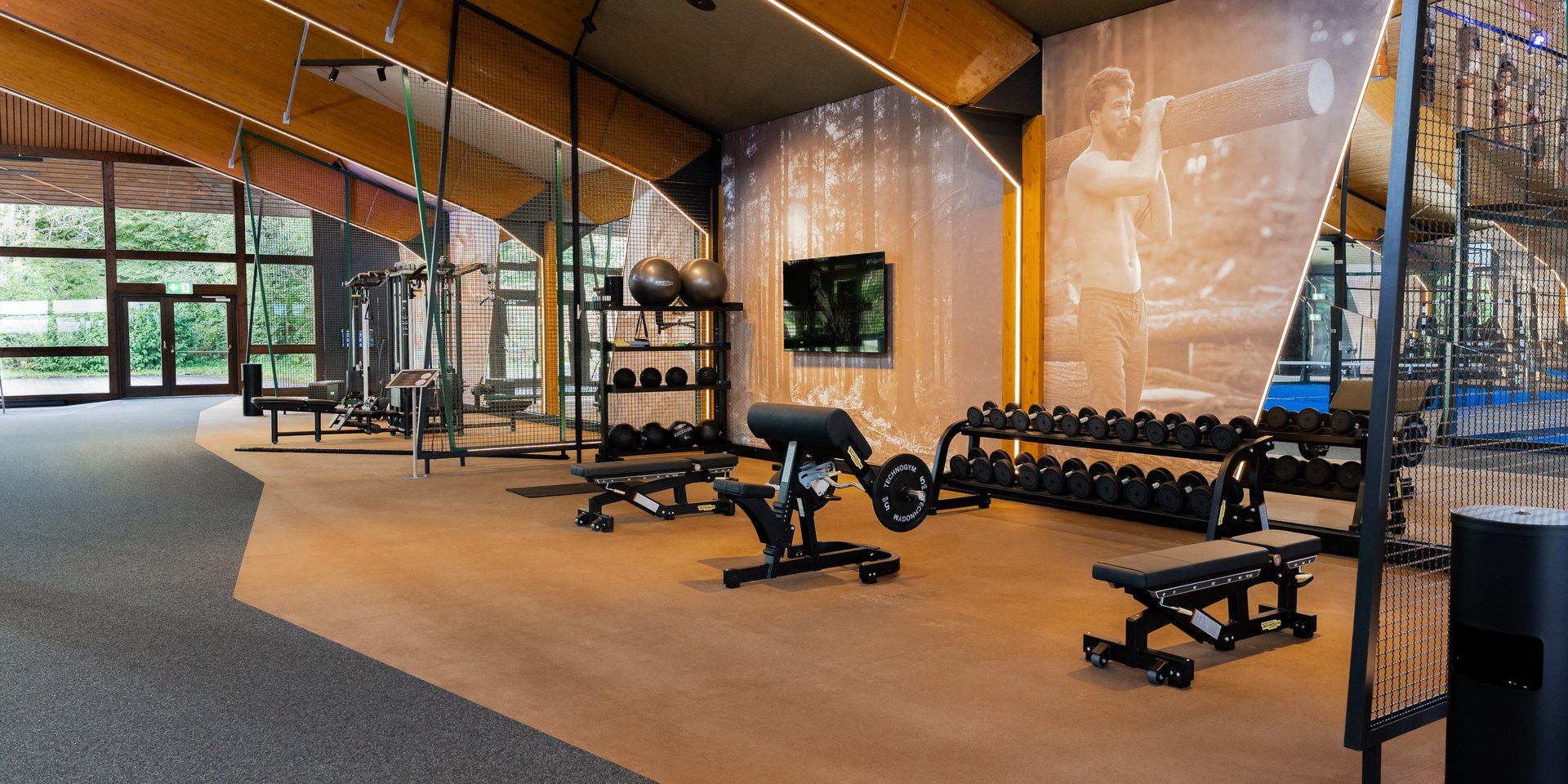 Großzügiger Hantelbereich und Trainingsbänke unter der markanten Holzdecke der hoteleigenen Sporthalle.
