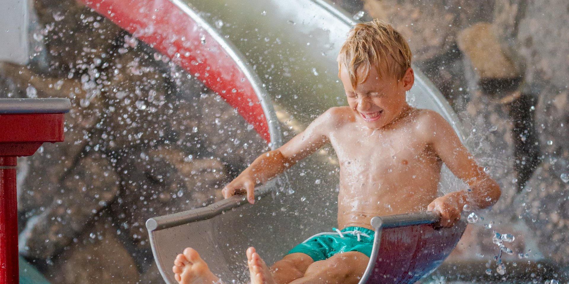 Ein kleiner Junge rutscht mit Schwung über eine Kinderrutsche direkt ins Wasserbecken des Hotels Vier Jahreszeiten.