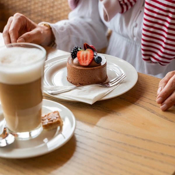 Detailaufnahme eines cremigen Latte Macchiato und eines Schokoladentörtchens auf einem Holztisch.