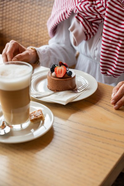 Detailaufnahme eines cremigen Latte Macchiato und eines Schokoladentörtchens auf einem Holztisch.