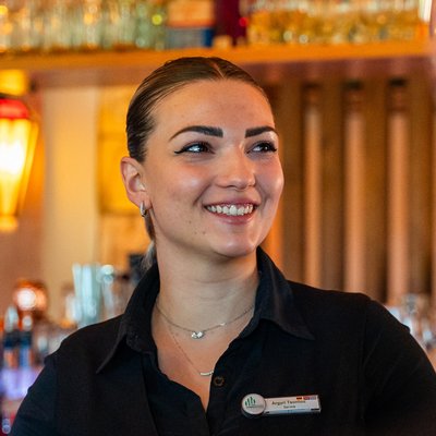 Eine herzliche Mitarbeiterin im Service des Hotels Vier Jahreszeiten im Schwarzwald im Gespräch mit einem Gast an der Bar.