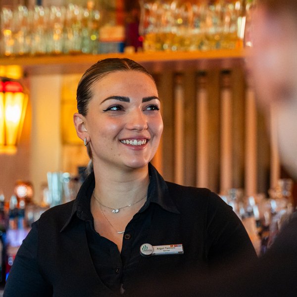 Eine herzliche Mitarbeiterin im Service des Hotels Vier Jahreszeiten im Schwarzwald im Gespräch mit einem Gast an der Bar.