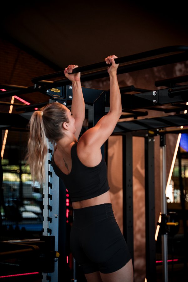 Eine Frau trainiert ihre Rückenmuskulatur durch Klimmzüge an der Sprossenwand.