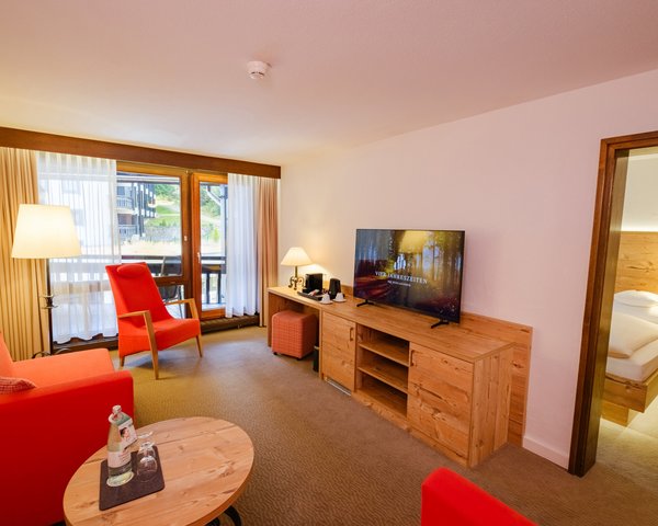 Wohnbereich der Suite mit rotem Sofa, Sessel und Blick in das angrenzende Schlafzimmer.