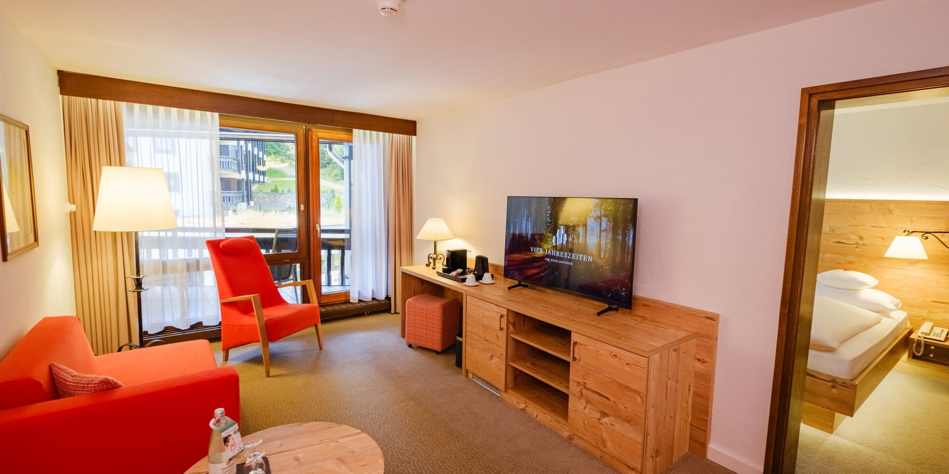 Wohnbereich der Suite mit rotem Sofa, Sessel und Blick in das angrenzende Schlafzimmer.