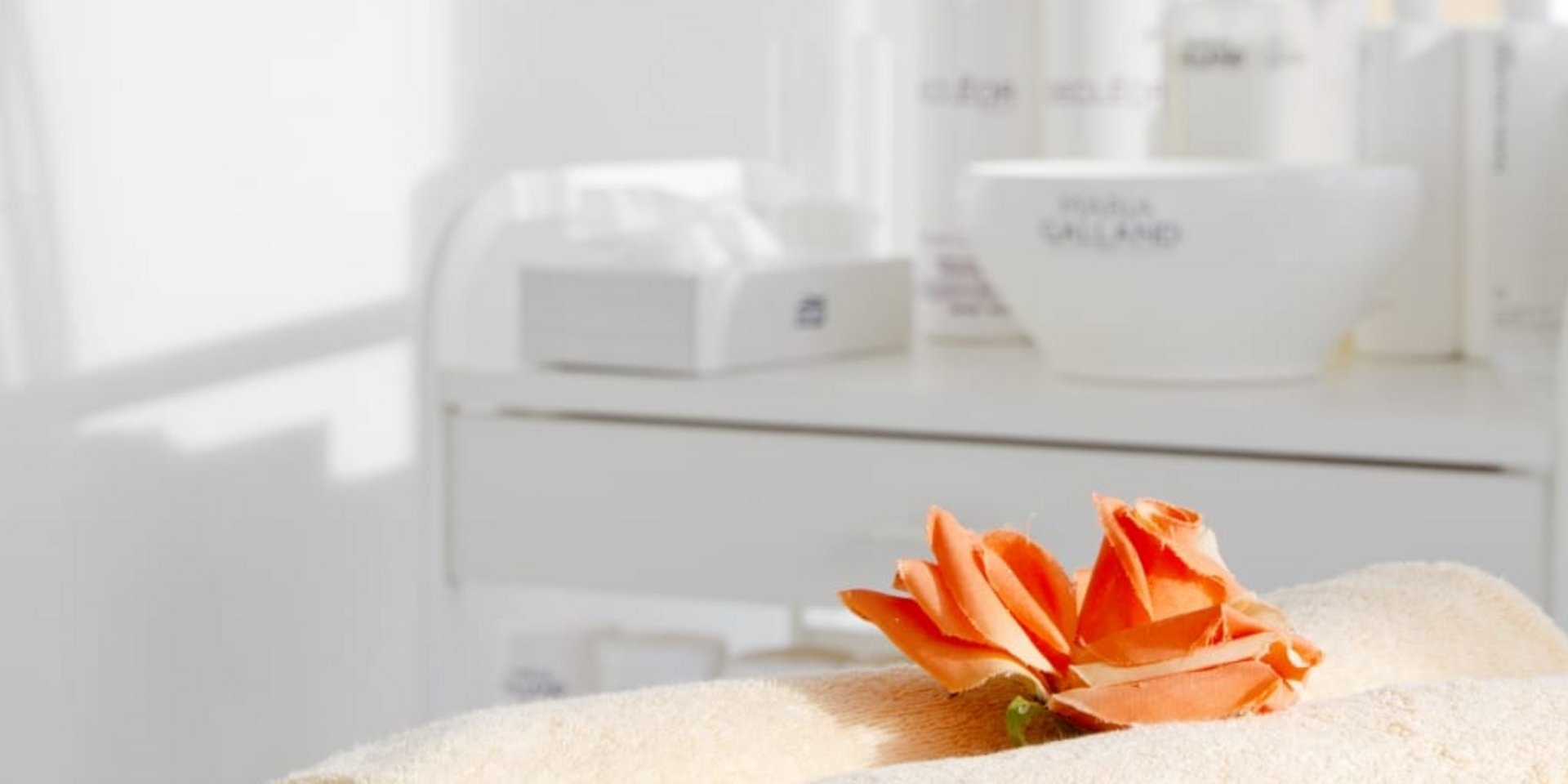 Frisch zusammengerollte, beige Handtücher mit einer dekorativen Blüte in einem hellen Behandlungsraum des Hotels Vier Jahreszeiten im Schwarzwald.