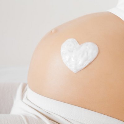 Ein Babybauch, auf den mit Creme behutsam ein Herz gezeichnet wurde.