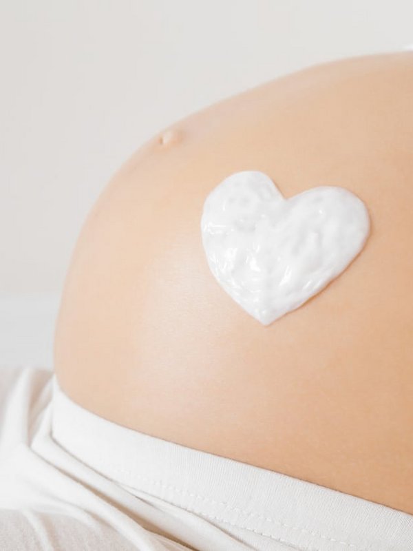 Ein Babybauch, auf den mit Creme behutsam ein Herz gezeichnet wurde.