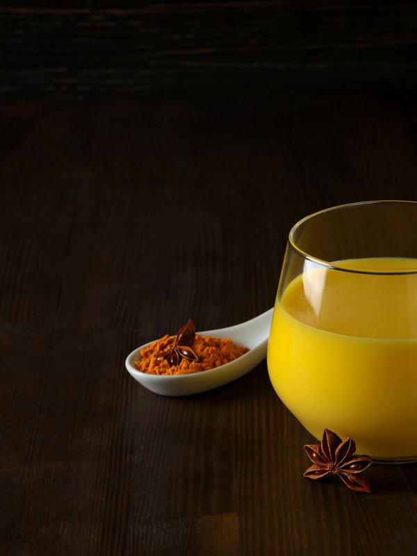 Ein Glas Saft steht auf einem Tisch daneben ein Löffel Kurkuma und vorne Sternanis