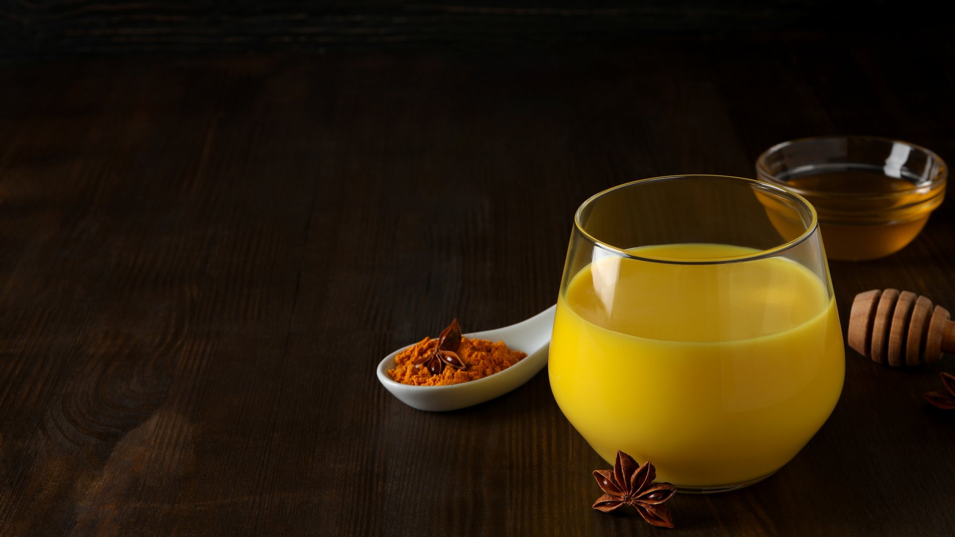 Ein Glas Saft steht auf einem Tisch daneben ein Löffel Kurkuma und vorne Sternanis