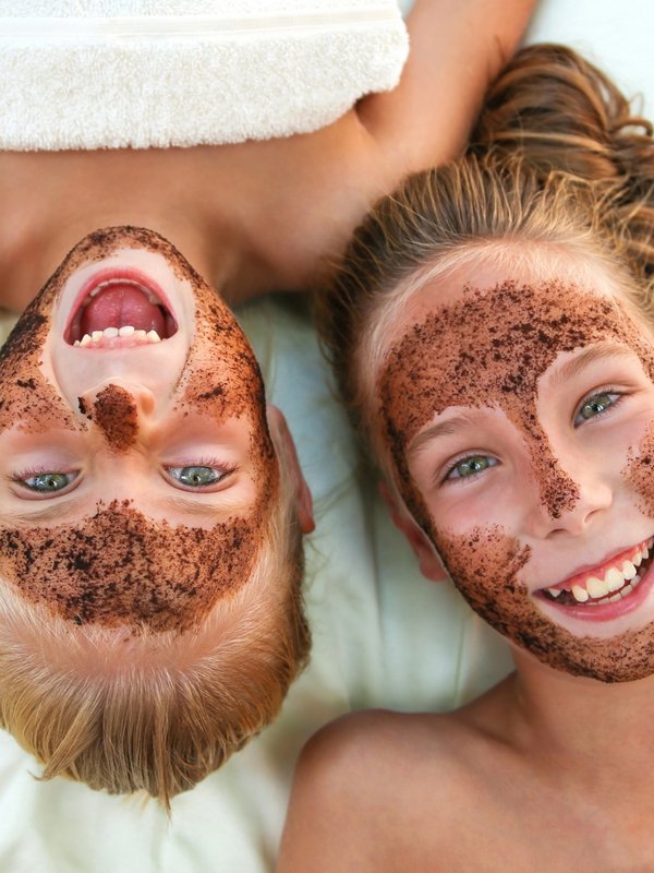 Zwei Kinder mit lustigen Gesichtsmasken aus Schokolade lachen während einer Wellness-Behandlung.