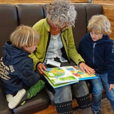 Eine Großmutter liest ihren zwei Enkeln in einer gemütlichen Sitzecke des Hotels Vier Jahreszeiten vor.