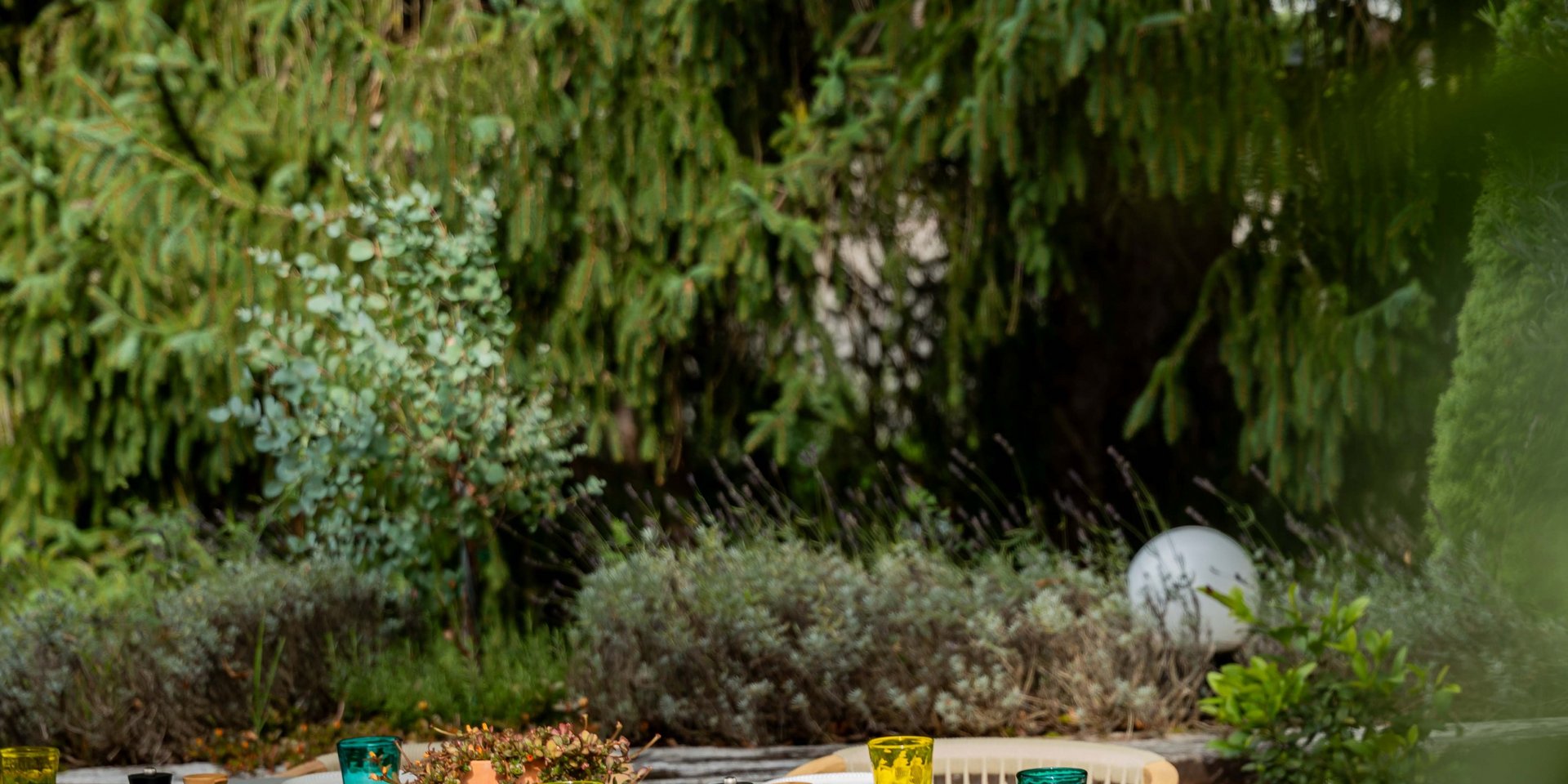 Mediterran gestaltete Außenterrasse des Restaurants Lucia mit rustikalen Holztischen im Grünen.