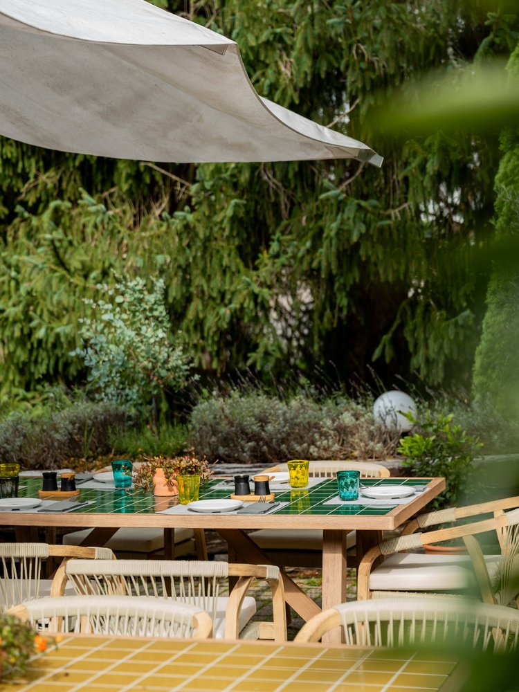 Mediterran gestaltete Außenterrasse des Restaurants Lucia mit rustikalen Holztischen im Grünen.