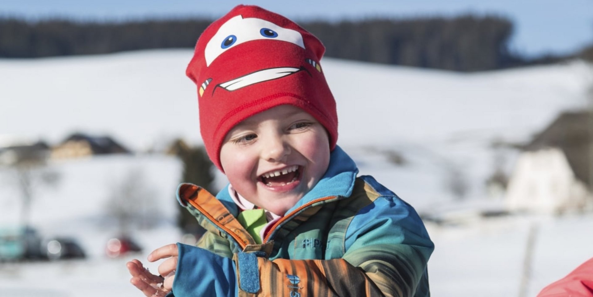 Ein fröhliches Kind lacht während einer Schneeballschlacht im Winterurlaub im Schwarzwald.
