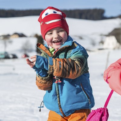 Ein fröhliches Kind lacht während einer Schneeballschlacht im Winterurlaub im Schwarzwald.