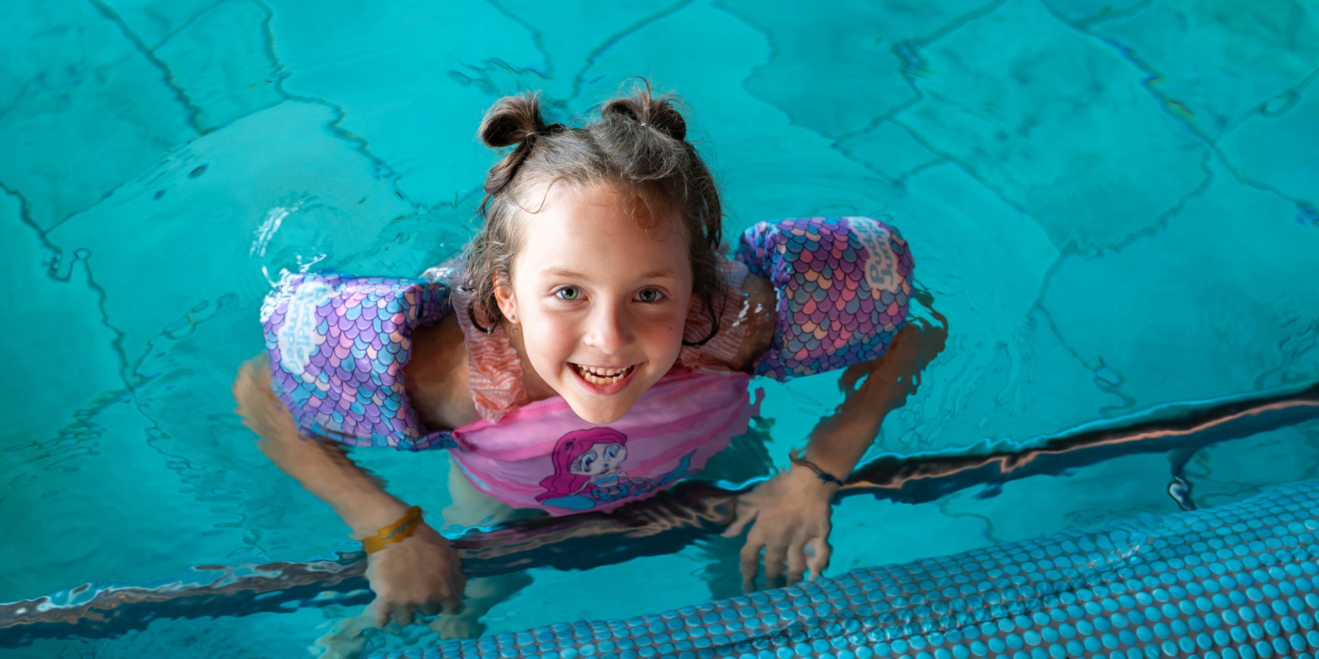 Mädchen mit Schwimmflügeln blick aus dem Pool