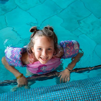 Mädchen mit Schwimmflügeln blick aus dem Pool