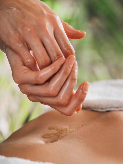 eine Person lässt aus Ihrer Hand Öl auf einen Bauch tropfen 