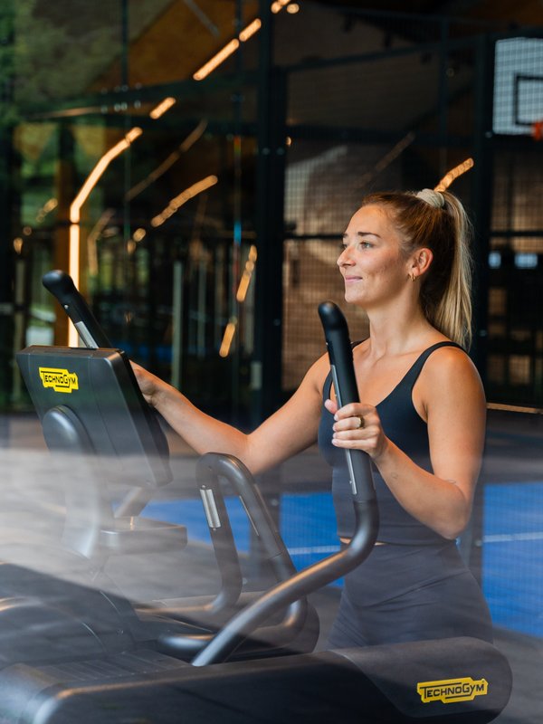 Eine Sportlerin nutzt den Crosstrainer im lichtdurchfluteten Fitnessbereich mit Blick nach draußen.