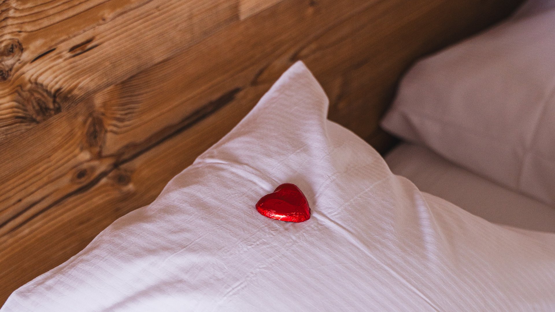 Detailaufnahme eines frisch bezogenen Hotelbetts mit einer dekorativen roten Blume auf dem Kissen.