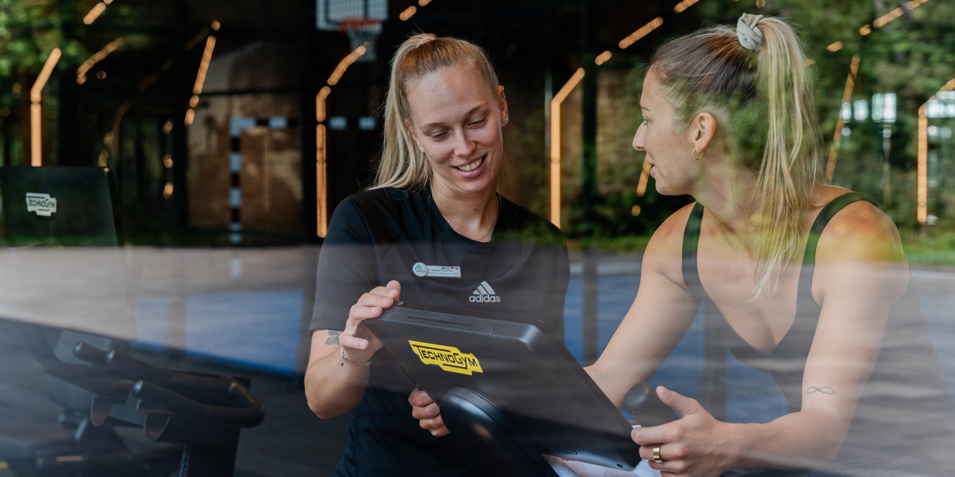 Eine Trainerin bespricht den individuellen Trainingsplan mit einem Gast an einem Tablet.