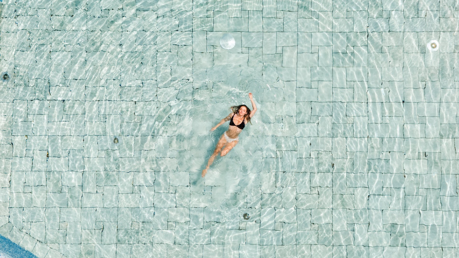 Frau schwimmt in Rückenlage im Außenpool