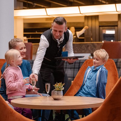 Ein Servicemitarbeiter im Hotel Vier Jahreszeiten am Schluchsee bedient freundlich eine Familie im Restaurant.