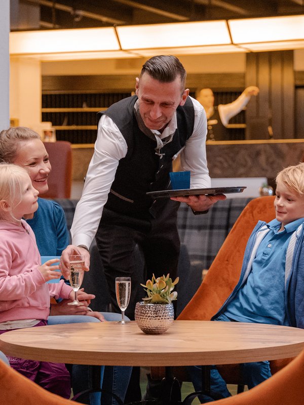 Ein Servicemitarbeiter im Hotel Vier Jahreszeiten am Schluchsee bedient freundlich eine Familie im Restaurant.