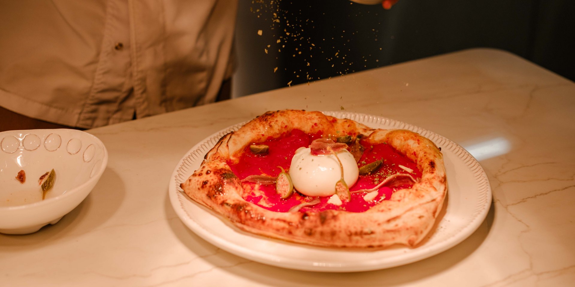 Eine frisch im Steinofen gebackene Pizza wird im Restaurant Lucia mit Gewürzen verfeinert.