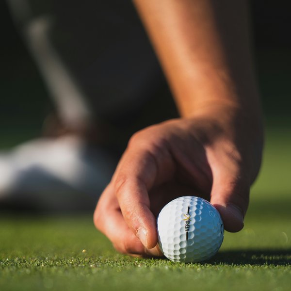 Detailaufnahme: Ein Golfspieler platziert konzentriert einen Golfball auf dem grünen Rasen im Hotel Vier Jahreszeiten am Schluchsee.