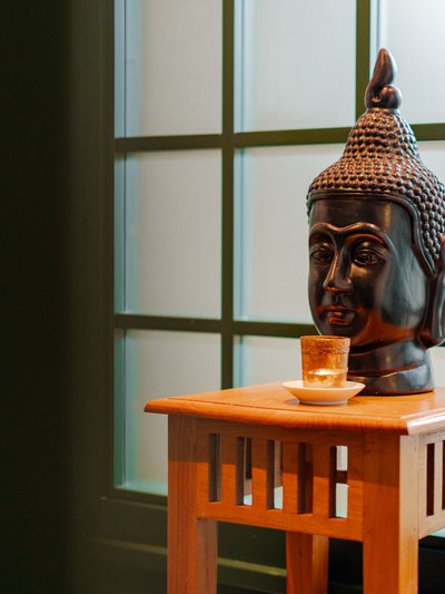 Ein Buddha-Kopf aus dunklem Stein auf einem kleinen Holzaltar vor einem Fenster im Hotel Vier Jahreszeiten am Schluchsee.