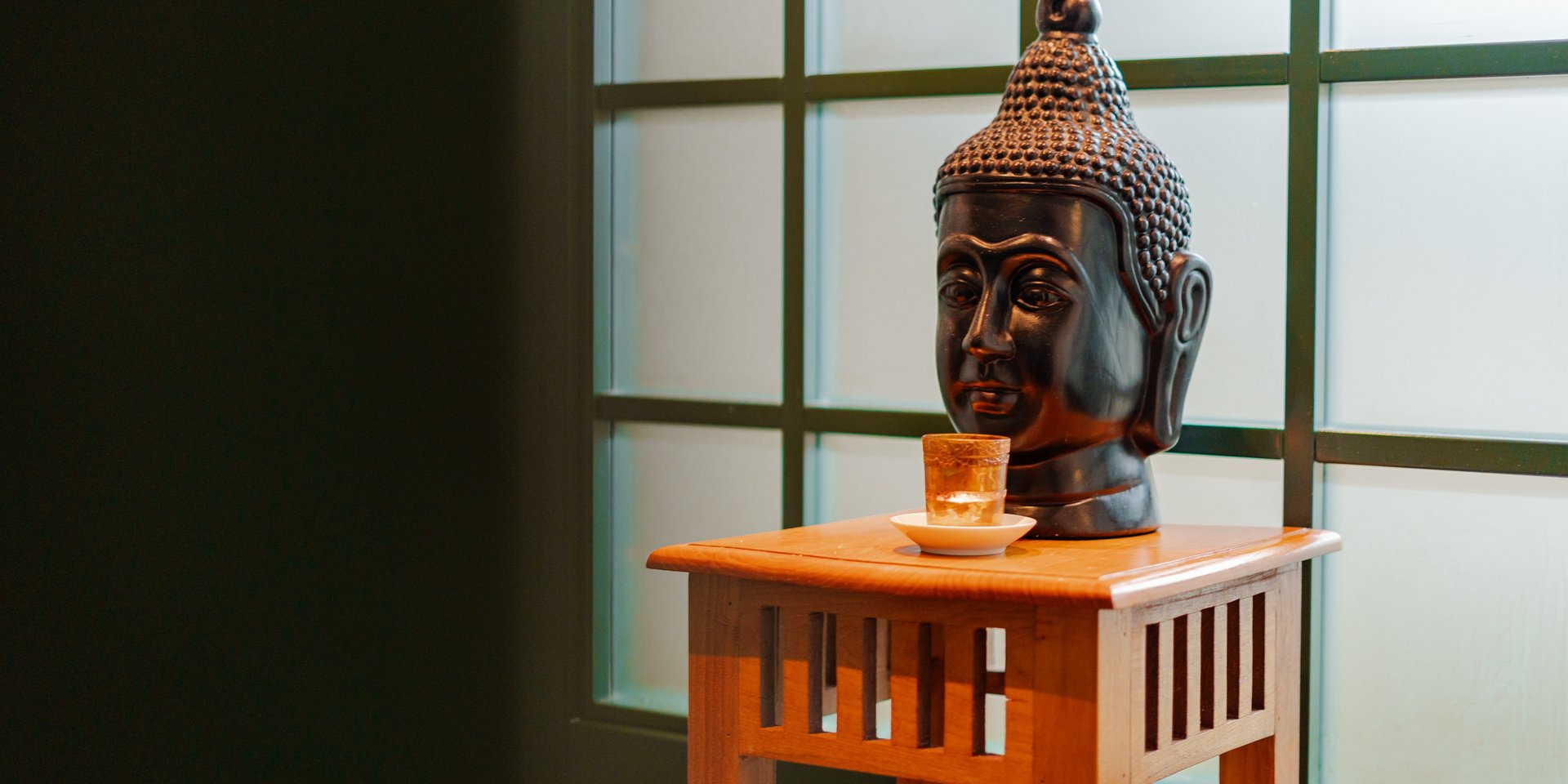 Ein Buddha-Kopf aus dunklem Stein auf einem kleinen Holzaltar vor einem Fenster im Hotel Vier Jahreszeiten am Schluchsee.
