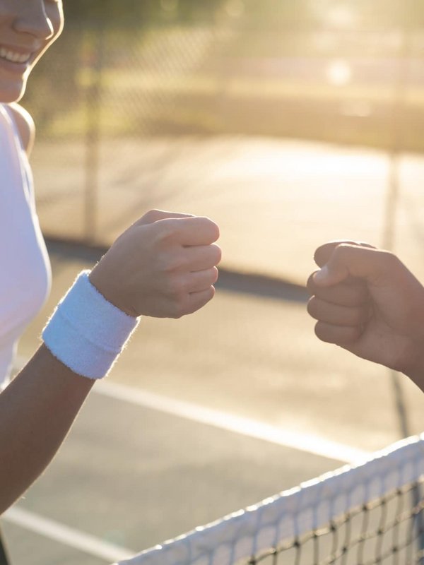 Zwei Tennisspielerinnen geben sich nach dem Match ein sportliches „Fist Bump“ am Netz.