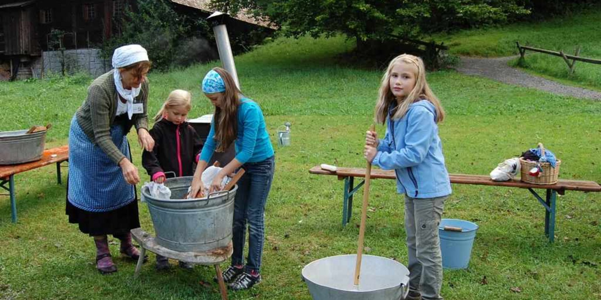 Handwerkliche Vorführung im Freien: Kinder und Erwachsene beim Buttern oder Waschen.