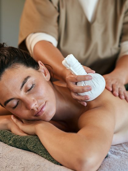 eine Frau liegt auf Ihre Hände gestützt und bekommt eine Kräuterstempel Massage