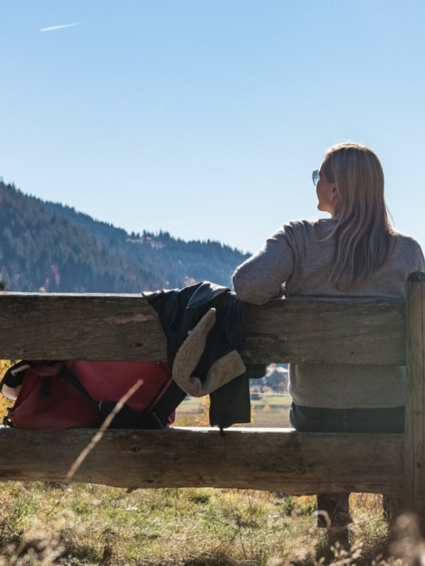 Eine Wanderin ruht sich auf einer Holzbank aus und blickt über den Schluchsee im Schwarzwald.
