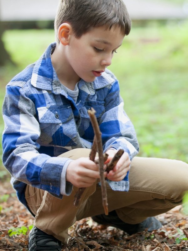 Ein Kind untersucht bei einem Natur-Workshop im Wald neugierig Pflanzen am Boden.