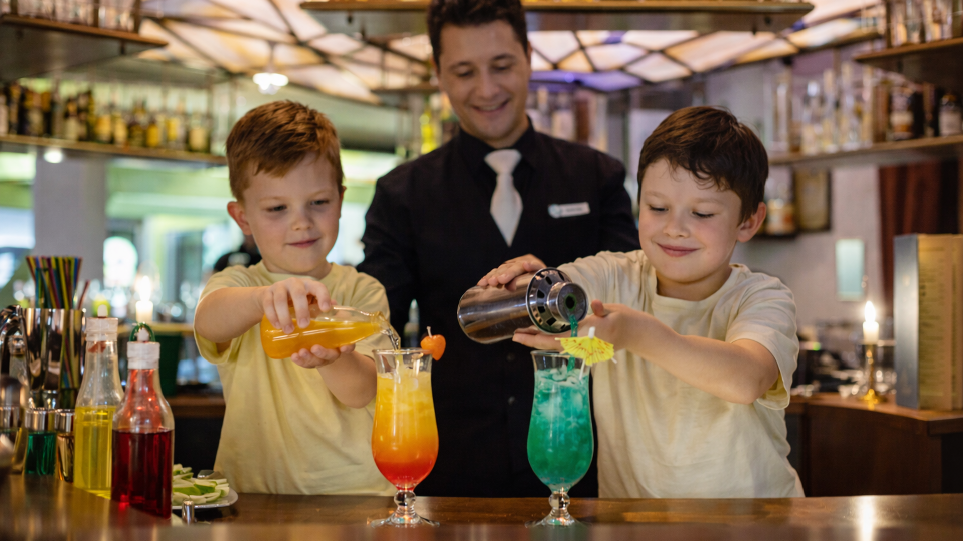 Ein Mann steht hinter zwei Kindern und zeigt Ihnen wie man Cocktails macht