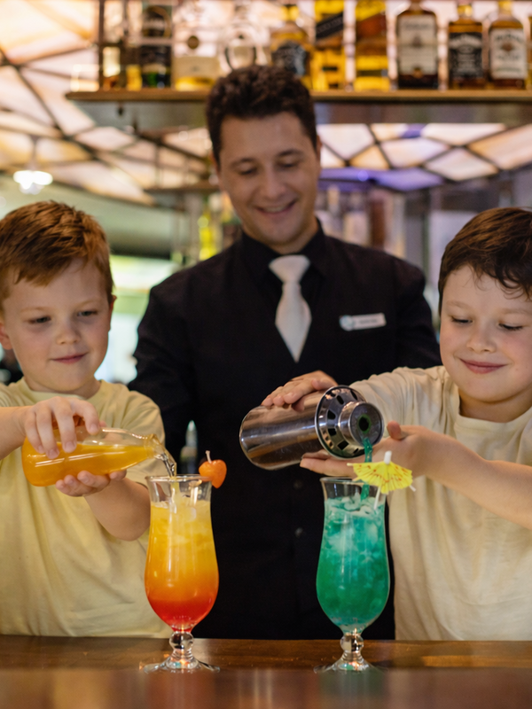 Ein Mann steht hinter zwei Kindern und zeigt Ihnen wie man Cocktails macht