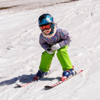 Ein Kind in bunter Skikleidung fährt konzentriert eine verschneite Piste hinunter.