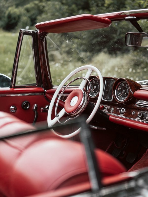 Blick in den Innenraum eines klassischen Oldtimer-Cabrios mit rotem Leder und Holzlenkrad.