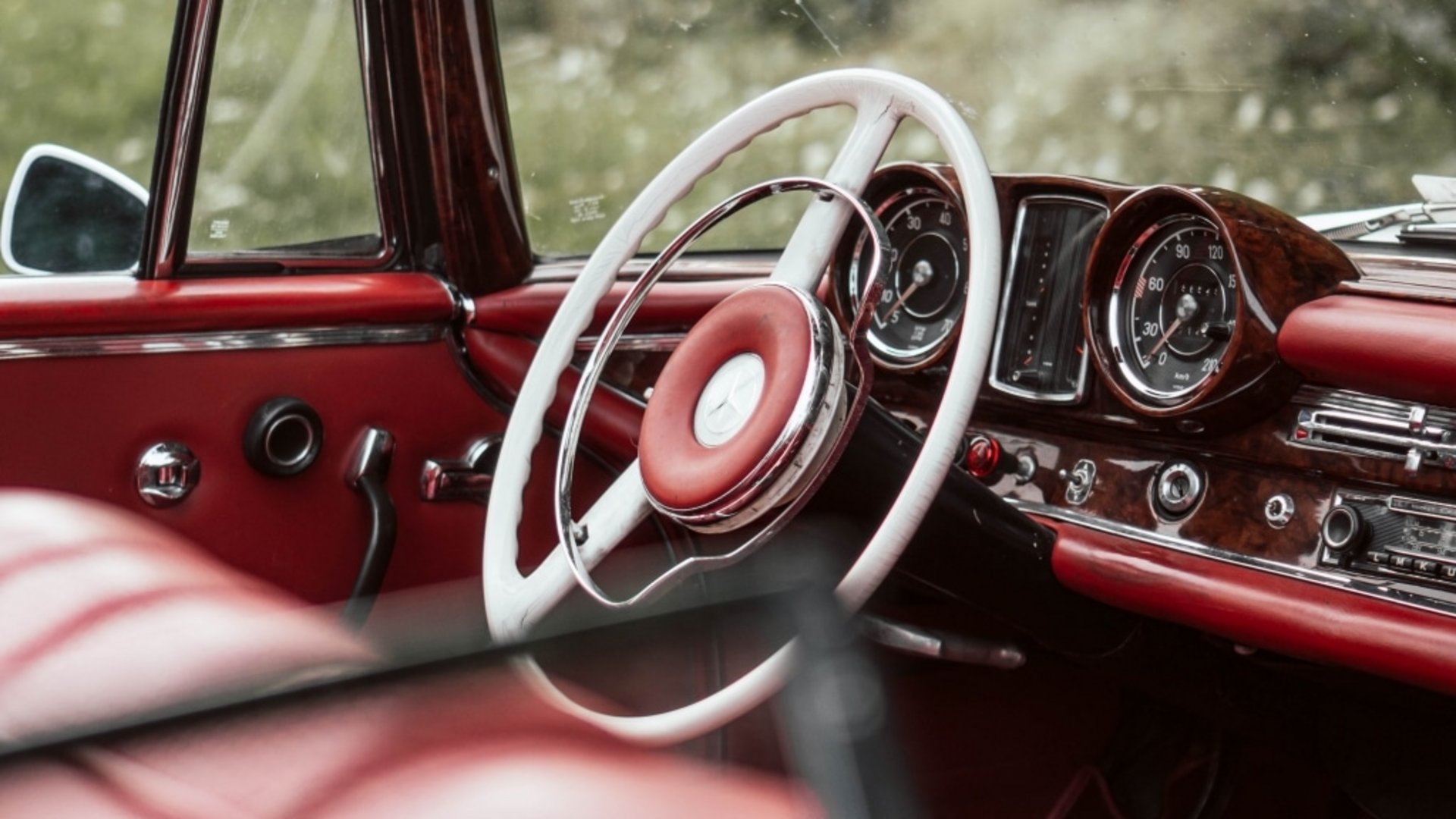 Blick in den Innenraum eines klassischen Oldtimer-Cabrios mit rotem Leder und Holzlenkrad.